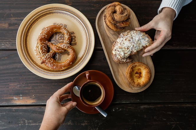 Hands holding coffee and a pastry.