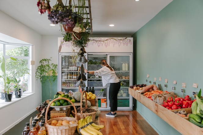 A woman looking in a fridge surrounded by fresh fruit and vegetables.