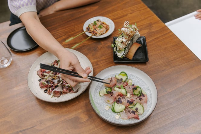Table of Japanese dishes from Bar Yoku with a person picking up a piece of sashimi with their chopsticks