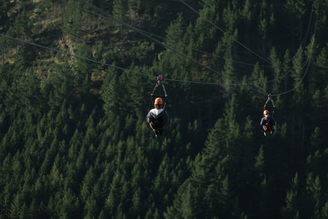 Two people ziplining above the forest in the Port Hills at Christchurch Adventure Park
