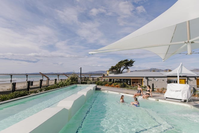 He Puna Taimoana hot pools overlooking New Brighton beach with a group of four women relaxing in the pool
