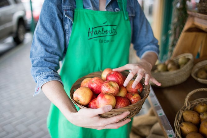 Person in green apron holding a basket full of local apples