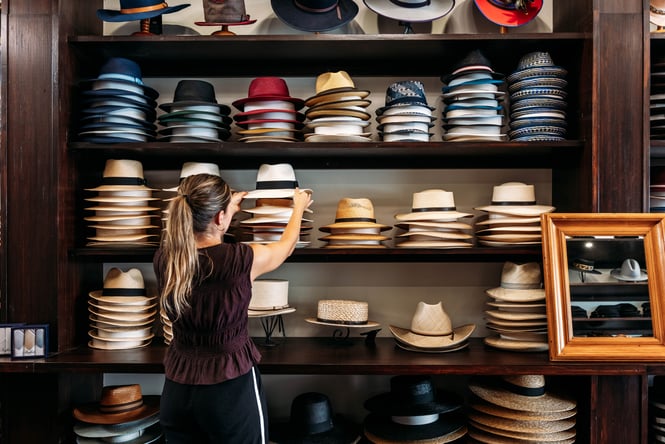 Woman picking up a hat off a pile in Hatlantis.
