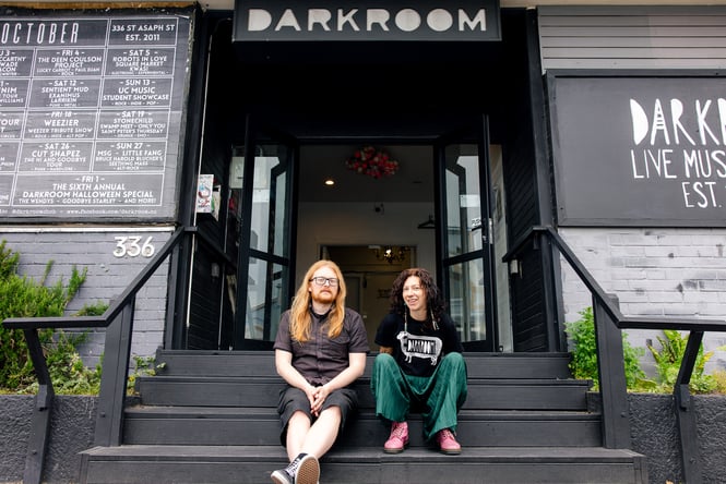 Two people sitting on black steps outside Darkroom bar Christchurch.