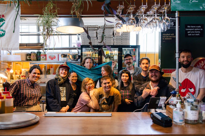 A group of people smiling to the camera from behind a bar.