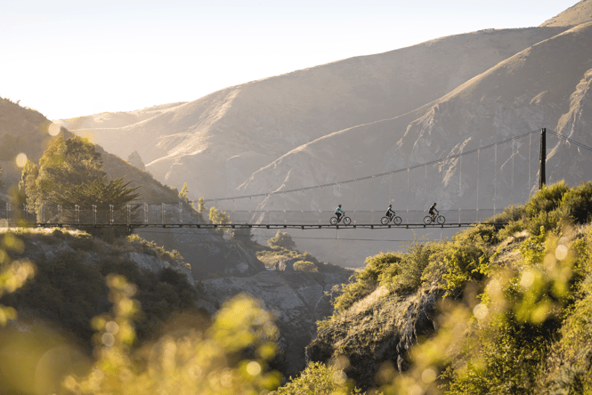 People biking on a swing bridge at dusk.