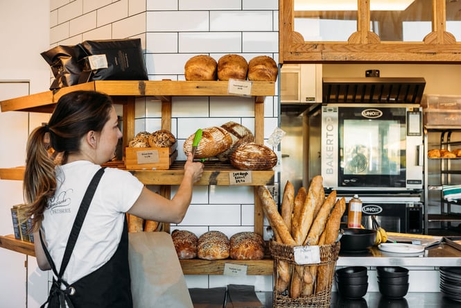 A staff member reaching for a loaf of bread with a pair of tongs.