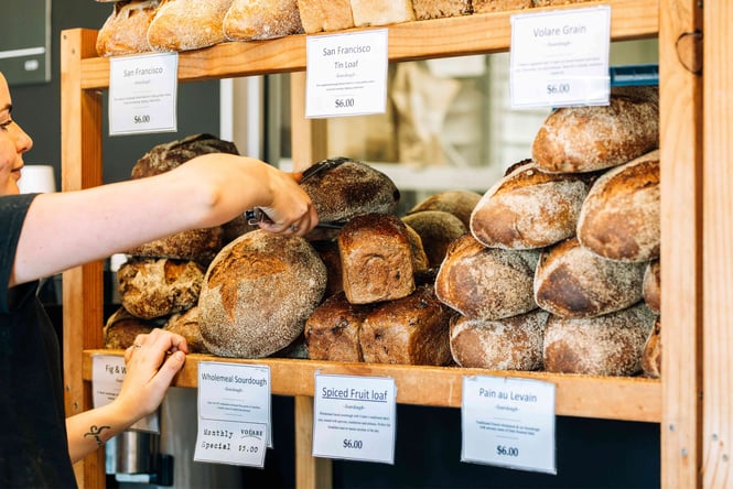 A woman reaching for a loaf of bread at Volare in Hamilton.