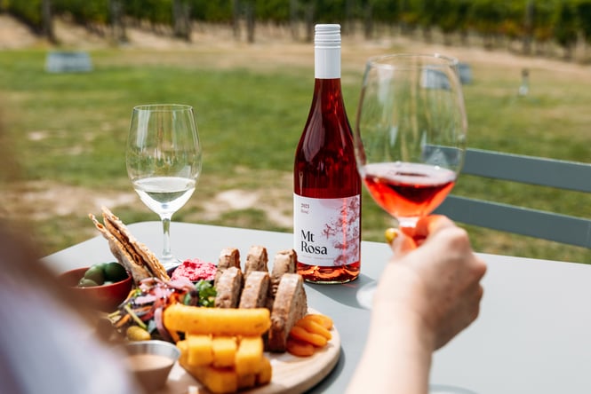 A hand holding a glass of wine next to a platter of cheese and crackers.