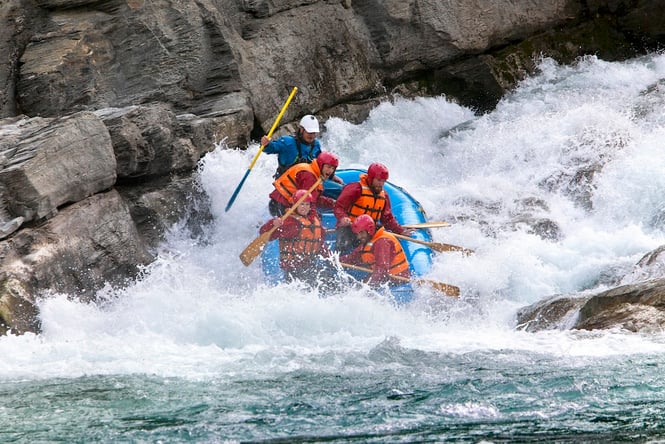 Five people in a raft going through whitewater rapids on the Shotover River.