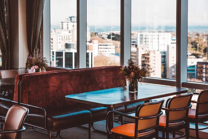 A table with a vase of dried flowers looking out big windows over Auckland city.