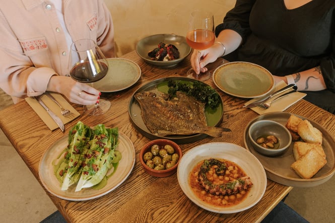 Two diners enjoying a glass of wine and a table full of elevated Spanish dishes from Odeon in Christchurch