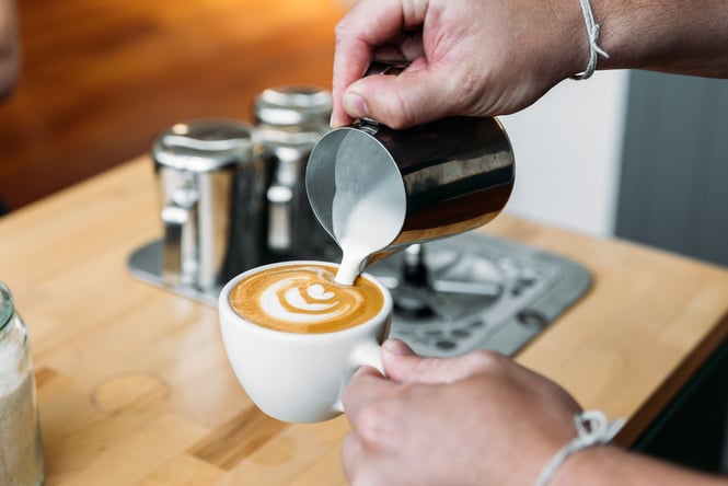 Close up of hands pouring frothed milk into a ceramic coffee cup.
