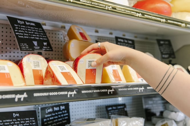 Someone picking up a packaged wedge of cheese from the deli section