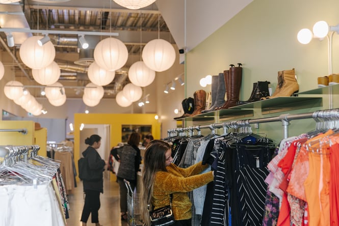 Young woman looking through rack of secondhand clothes at Recycle Boutique