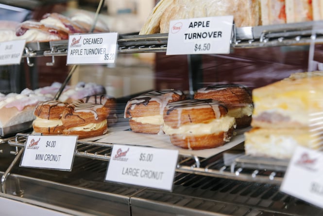 A close up of a tray of donuts on display behind glass.