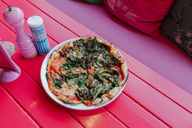 Close up of a pizza on a pink table.