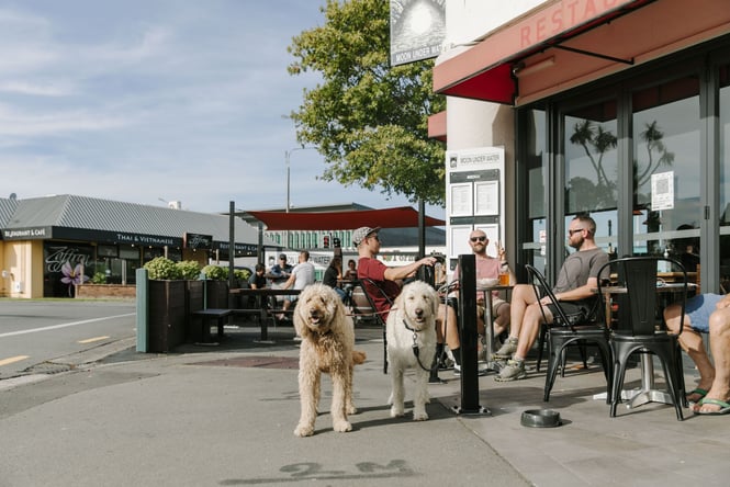 Two dogs and a group of people sitting outside Moon Under Water on a sunny day.