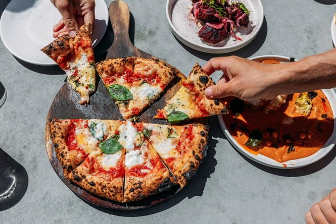 Hands reaching for a pizza.