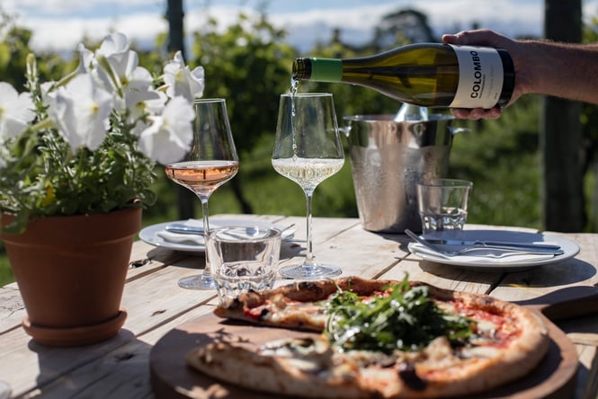 Wine and pizza on a table outside.