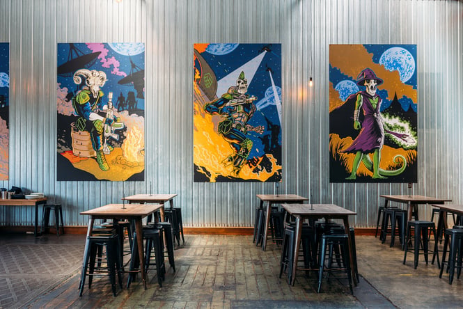 Tables and chairs against a large wall with works of art on display.