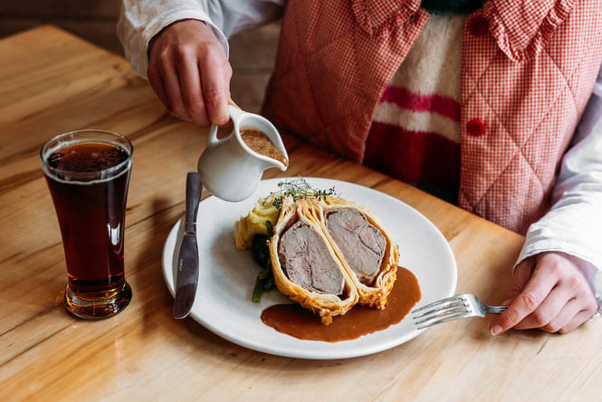 Someone pouring gravy over a beef wellington dish from Danseys Pass Hotel