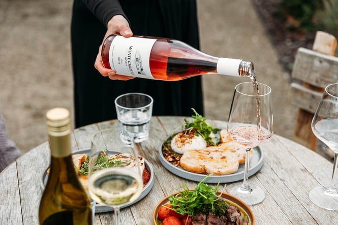 Rose wine being poured from the bottle next to fresh seasonal dishes at Monte Christo