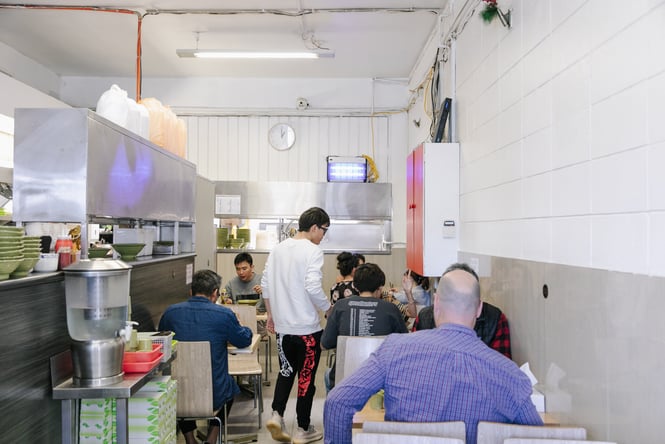 Customers dining at tables inside a simply decorated Eden Noodles restaurant.