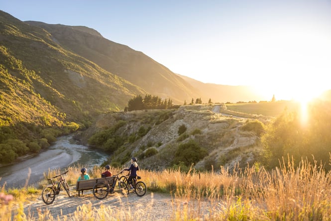 People with bikes on a hill at sunset.