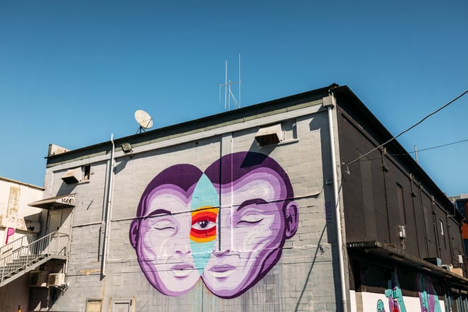 A purple and blue mural of a face on a concrete wall.