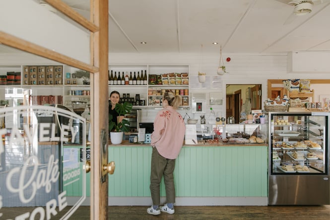 A woman wearing a pink jacket and green pants standing at the cafe counter.
