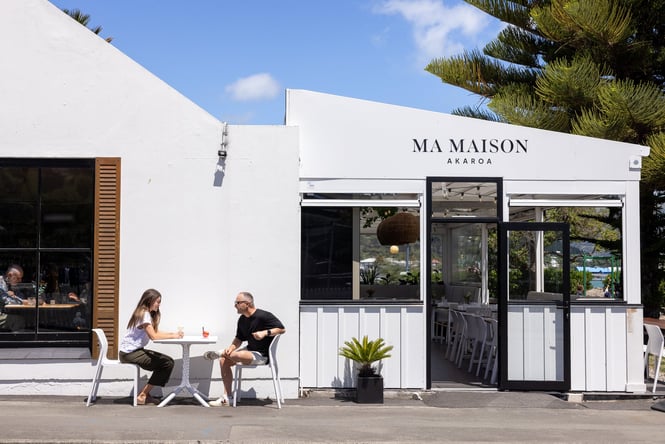 Two people sitting outside Ma Maison restaurant on a sunny day in Akaroa