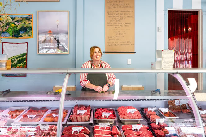 Julia standing behind cabinet of quality NZ meat at Akaroa Butchery