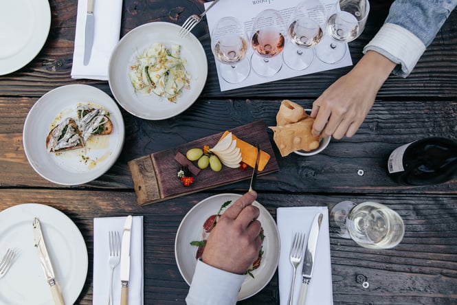 A flat lay of hands reaching for food on a wooden table.