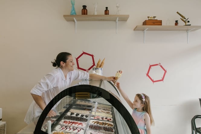 A girl reaching for a gelato over the counter.