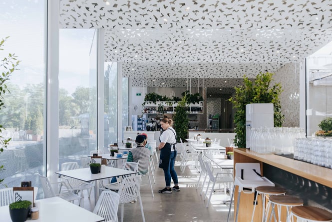 A staff member talking to customers seated at white table and chairs inside Ilex cafe in Christchurch.