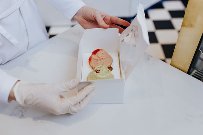 A close up of two small cakes in a white box.