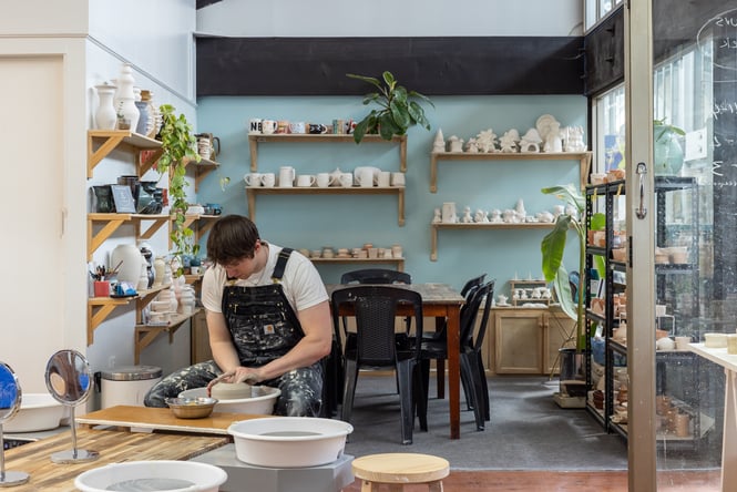 Interior of Pottery Capital with potter throwing clay with shelves of ceramics in the background