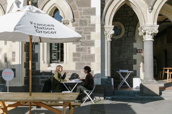 Two women sitting outside Frances Nation Grocer on a sunny day.