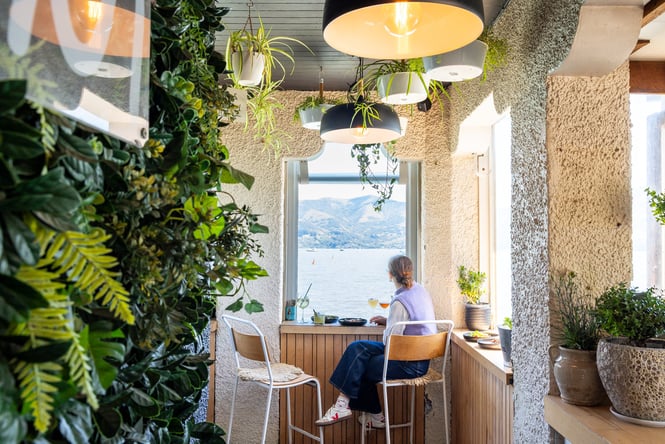Person looking out small window with waterfront views at Tini in Akaroa