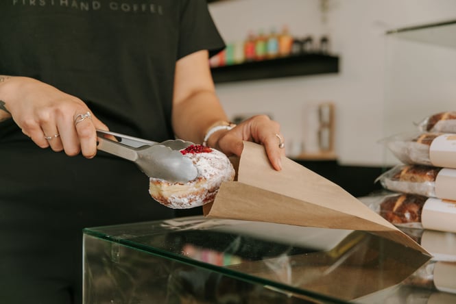 A cream bun being put into a bag.