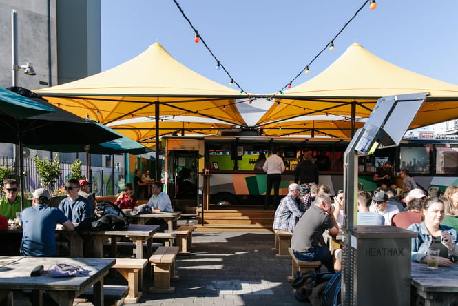 Sunny day at Smash Palace bar with tables full of people drinking under umbrellas