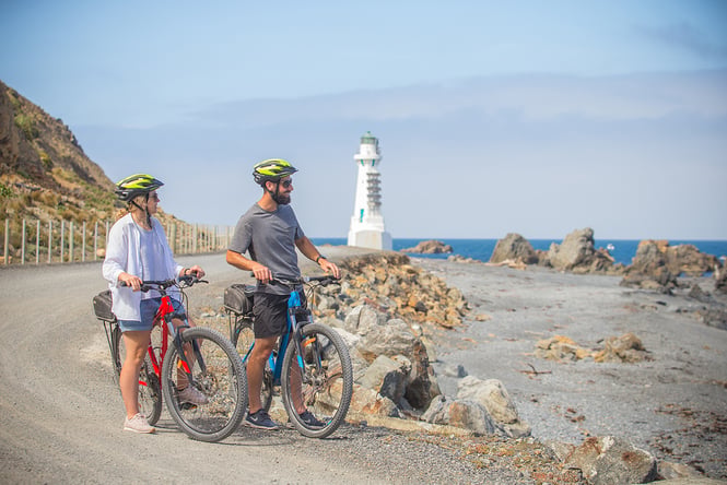 Two people looking out towards the ocean whilst leaning on bikes. Photo by WellingtonNZ.