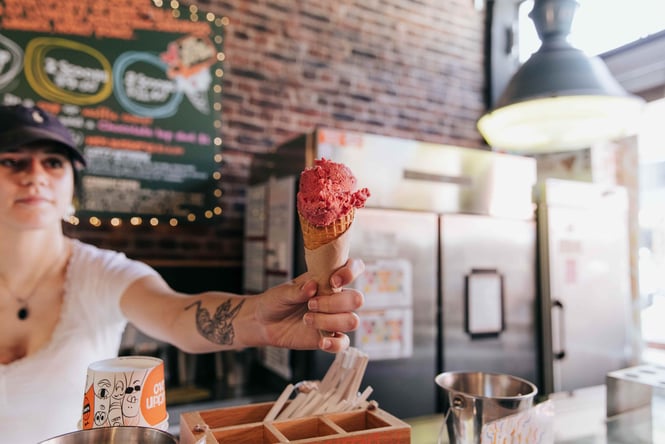 A female staff member passing a gelato cone over the counter.