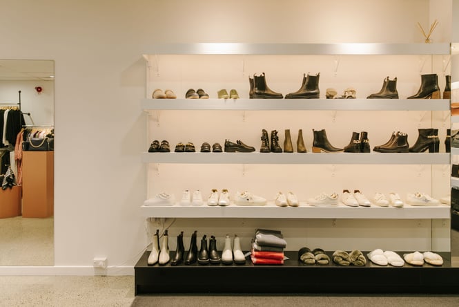 Shoes and woollen scarves on display on white shelves.