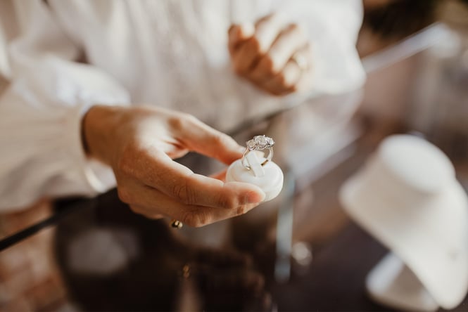 A hand holding a diamond ring in a box.