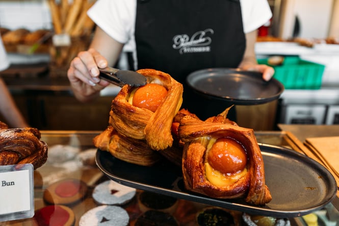 Close up of someone putting a glossy apricot danish into a brown paper bag