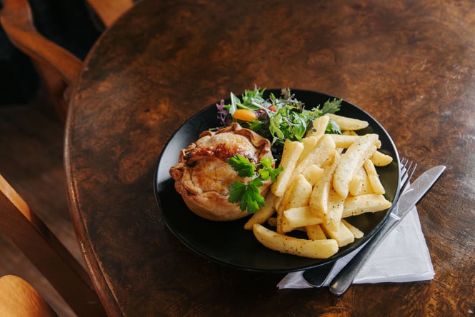 A pie and hot chips on a black plate.