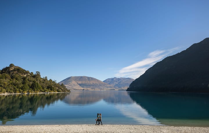 Two people walking along a lake on a sunny day.