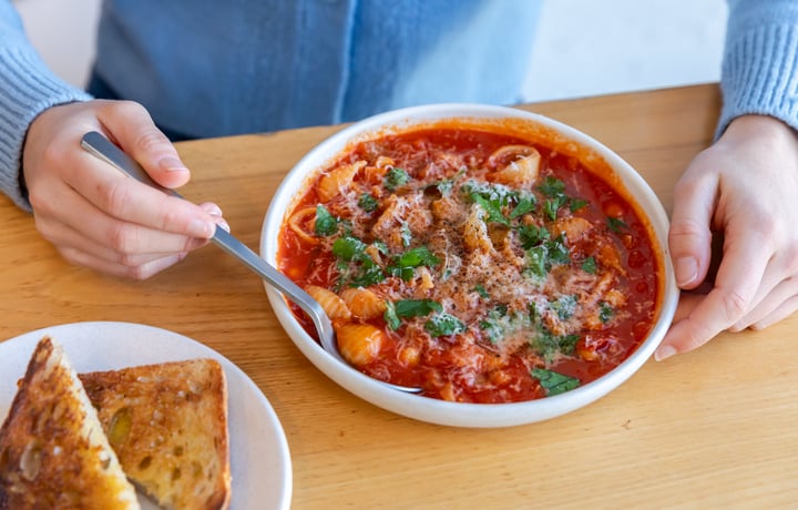 Close up of someone dipping spoon into minestrone soup from Estelle next to plate of toast